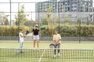 Young sporty woman with children playing padel game in court on sunny day photo