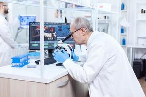 Senior scientist preparing and analyzing microscope slides with busy coworkers. Chemist researcher in sterile lab doing experiments for medical industry using modern technology. photo