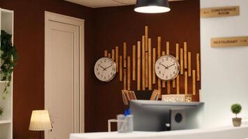 Empty cozy check in front desk in stylish luxurious resort lounge interior filled with plants and clocks on wall. Welcoming hotel reception counter ready for arriving guests photo