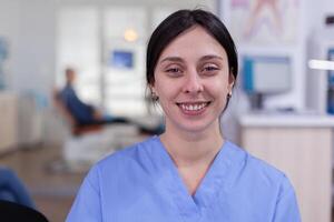 Smiling stomatology nurse looking at camera in dentist office wainting area, senior man waiting for teeth health examination. Dentistiry woman sitting on chair. photo