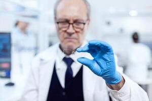 cerca arriba de medicina muestra en vaso diapositiva mientras científico es mirando a eso en laboratorio. mayor investigador en estéril laboratorio mirando en microscopio diapositiva vistiendo laboratorio abrigo. foto