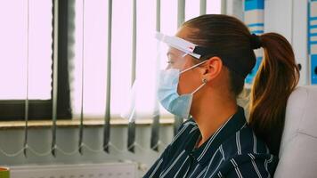 Portrait of businesswoman wearing protection mask and visor typing and talking with colleague working in new normal business office respecting social distance during global pandemic. photo