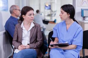 Nurse taking notes on clipboard about patient dental problems waiting for orthodontist sitting on chair in waiting room of stomatological clinic. Assistant explaining medical procedure to woman. photo