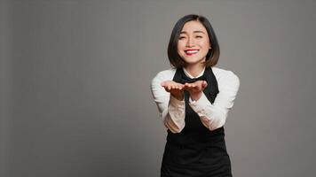 Cute flirty waitress blowing air kisses in front of camera, acting romantic with sweet gesture. Asian restaurant employee posing with a kissy facial expression, catering industry. Camera A. photo