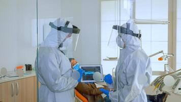 Dentist doctors in overall using tablet explaining dental x ray in stomatologic office during coronavirus. Man wearing face shield and mask showing to nusrse radiography using digital device photo