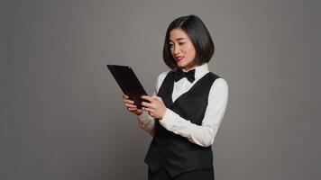 Asian hotel administrator browsing online website to check all reservations or room bookings, smiling and being confident. Receptionist using tablet in studio, hospitality industry. Camera A. photo