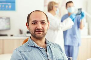 Closeup of patient man looking into camera waiting for doctors to start stomatology surgery sitting on dental chair. Senior doctor and medical nurse examining teeth radiography photo