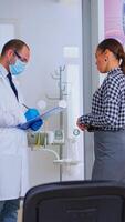 Doctor taking notes on clipboard about woman dental problems standing in waiting area, while nurse preparing tools for next patient in consultation room. Dentist explaining medical procedure. photo