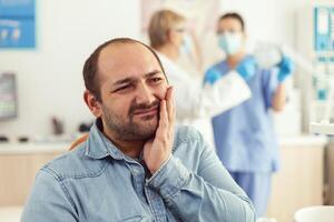 Man patient visiting stomatology cabient complaining about toothache during orthodontic appointment. Hospital team looking at teeth radiography examining dental problems during dentistry appointment photo