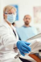 Closeup of stomatologist doctor preparing dental tools for stomatology surgery during dentistry appointment. Orthodontist medic wearing face mask discussing with man patient for medical treatment photo