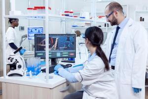 Group of scientist analysing genetic material. Team of researchers doing pharmacology engineering in sterile laboratory for healthcare industry with african assistant in the background. photo