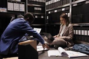 Police officers searching for new evidence in arhive room, discussing crime scene report working at criminal investigation. Diverse private detectives analyzing criminology files, checking every clue photo