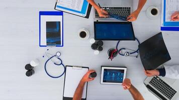 Group of doctors working together, taking notes and analysing x-ray on top view copy space sitting on desk with stethoscope and digital device all around having medical conference. photo