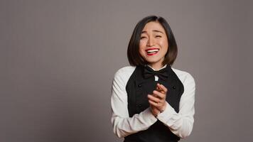 Asian server applauding someone and cheering for success, saying congratulations in front of camera. Waitress in formal uniform clapping hands, doing standing ovation gesture. Camera B. photo