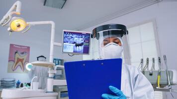 Pov of patient getting dental treatment in dentist office with new normal, doctor taking notes on clipboard before examining. Stomatolog wearing safety gear against coronavirus during heatlhcare check photo