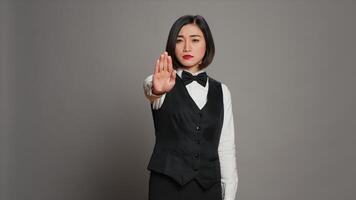 Asian administrator showing stop sign with palm raised in studio, presenting negative symbol and expressing disapproval. Woman receptionist doing no gesture, being displeased. Camera A. photo
