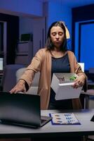 Deprimido empleado después siendo despedido con caja de tarjetas en manos. triste mujer participación su pertenencias tarde a noche en el oficina después siendo despedido desde trabajo. despedido mujer de negocios, economía crisis foto