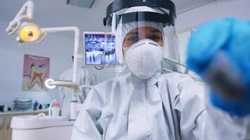 Patient pov of dentist holding dental tools wearing covid protection suit treating patient in new normal clinic. Stomatolog wearing safety gear against coronavirus during heatlhcare check of person. photo