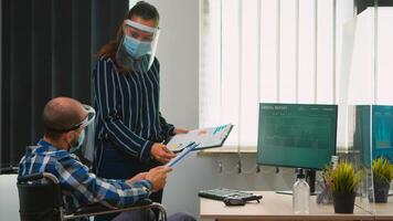 Businesspeople crew with face protection against coronavirus, working at startup project in new normal loft. Team consulting in professional workplace looking at desktop respecting social distance photo