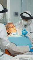 Woman at dentist while treatment process in coronavirus pandemic lying on stomatological chair. Doctor and nurse working wearing coverall, face shield, protection suit, mask, gloves in dental office photo