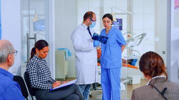 Dentist showing teeth x-ray reviewing it with nusre. Doctor and assistant working in modern crowded stomatological clinic, patients sitting on chairs in reception filling in dental forms and waiting photo