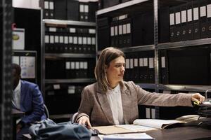 Investigator analyzing police report, checking crime case confidential information. Private detective in formal suit discovering mysterious victim files, working overtime in arhive room photo