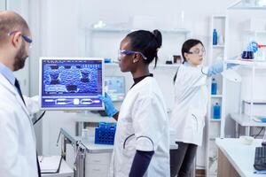 Multiethnic team of medical researchers working together in sterile lab wearing protection glasses and gloves. photo