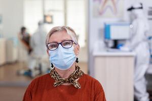 Portrait of retired patient in dental office looking on camera wearing face mask sitting on chair in waiting room clinic while doctor working. Concept of new normal dentist visit in coronavirus outbreak. photo