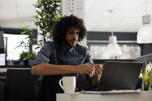 joven árabe negocio profesional que se discute proyecto en en línea reunión utilizando ordenador portátil en comienzo arriba oficina. ejecutivo gerente chateando acerca de márketing estrategia en videollamada con remoto equipo foto