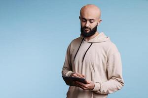 Arab man using digital tablet application, browsing internet and writing online message. Young person texting in social media and while tapping on portable gadget touchscreen photo