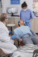 Assistant woman applying anesthesia with cotton swab before stomatological surgery in orthodontic office room. Medical team discussing treatment against caries infection during dentistry examination photo