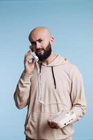 Confused arab man talking on landline phone and looking at camera with uncertain expression. Young person in doubt having conversation, answering vintage telephone call portrait photo