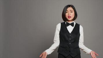 Bored receptionist being confused and overworked in studio, posing with confusion and fatigue over grey background. Asian administrator feeling uncertain and unsure about something. Camera A. photo