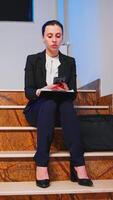 Exhausted tired businesswoman working on project deadline using smartphone sitting on staircase of business building. Serious entrepreneur working on corporate job texting late at night. photo