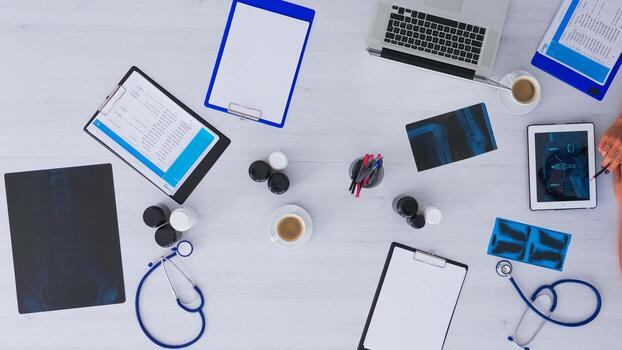Top view of medical student learning using digital program on tablet with x-ray, clipboards and medical equipment all around. Studying in hospital office, copy space, flat lay concept photo
