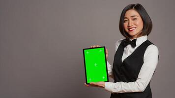 Woman concierge presenting greenscreen display on tablet, showing chromakey template on screen. Receptionist with bow and uniform holding device with blank copyspace layout. Camera B. photo