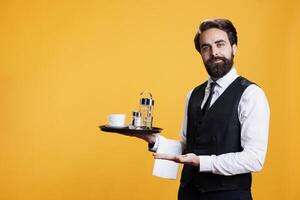 Waiter employee presenting ad aside and carrying restaurant tray, working as luxurious personnel to serve clients. Young man with formal attire creating advertisement pointing to sides. photo