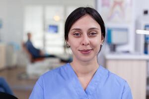 Smiling stomatology nurse looking at camera in dentist office wainting area, senior man waiting for teeth health examination. Dentistiry woman sitting on chair. photo