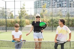 Young sporty woman with children playing padel game in court on sunny day photo