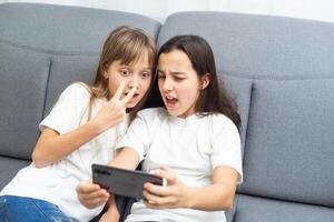 people, technology and friendship concept - happy teenage girls taking selfie with smartphone sitting on sofa at home photo