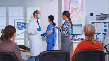 Doctor taking notes on clipboard about woman dental problems standing in waiting area, while nurse preparing tools for next patient in consultation room. Dentist explaining medical procedure. photo