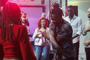 African american couple showing moves on crowded dancefloor in nightclub. Man and woman carefree dancers improvising dance battle for young people at discotheque party in club photo