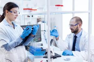 grupo de científico conductible y Ingenieria genético material análisis. equipo de químico farmacia trabajando juntos en estéril microbiología laboratorio haciendo investigación. foto