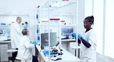 Multiethnic scientists team working together in modern facility doing virus analysis. Black healthcare researcher in biochemistry laboratory wearing sterile equipment. photo