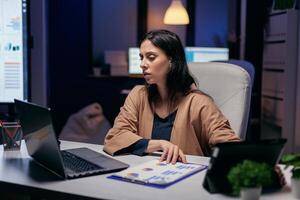 Entrepreneur reading project deadline for important client using tablet pc and laptop. Business woman working overtime at the office to finish a corporate job using tablet pc. photo