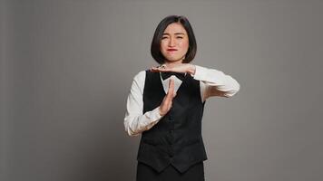 Front desk employee asking for a break in studio, showing timeout symbol and feeling overworked. Tired asian receptionist dealing with burnout and asking for a pause. Camera A. photo