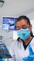 Patient pov in dental office explaining treatment of teeth cavity, dentist pointing on x-ray image. Stomatology doctor wearing protective mask and gloves, working in modern stomatological clinic photo