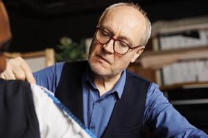 Client getting arm measurements taken by precise elderly suitmaker in tailoring shop. Skilled senior couturier sizing up gentleman proportions for handmade bespoke suit piece comission, close up photo