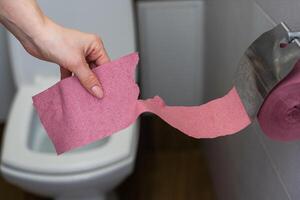 A female hand, woman holding a roll of pink toilet paper, digestive problems and defecation disorder concept. photo