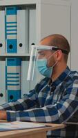 Handicapped businessman with visor and protection mask working in new normal business office. Man discussing with colleague in financial company respecting social distance during global pandemic. photo